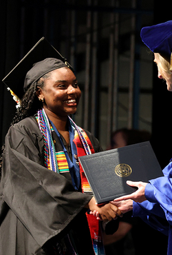 A graduate in cap and gown shakes hands with UIS Chancellor Janet Gooch while holding a diploma cover on stage.