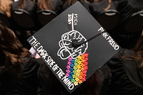 graduation cap with text Pink Freud: Dark Side of the Brain and a black and white brain with a rainbow of flowers coming out of it like a prism