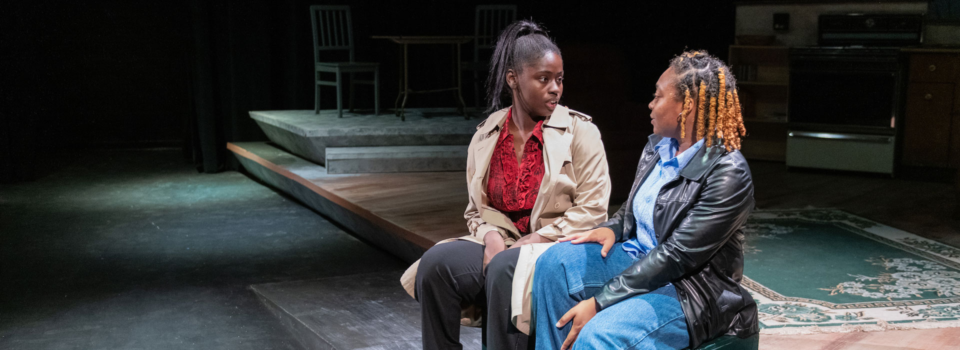 two people sitting on stage in a play talking to each other