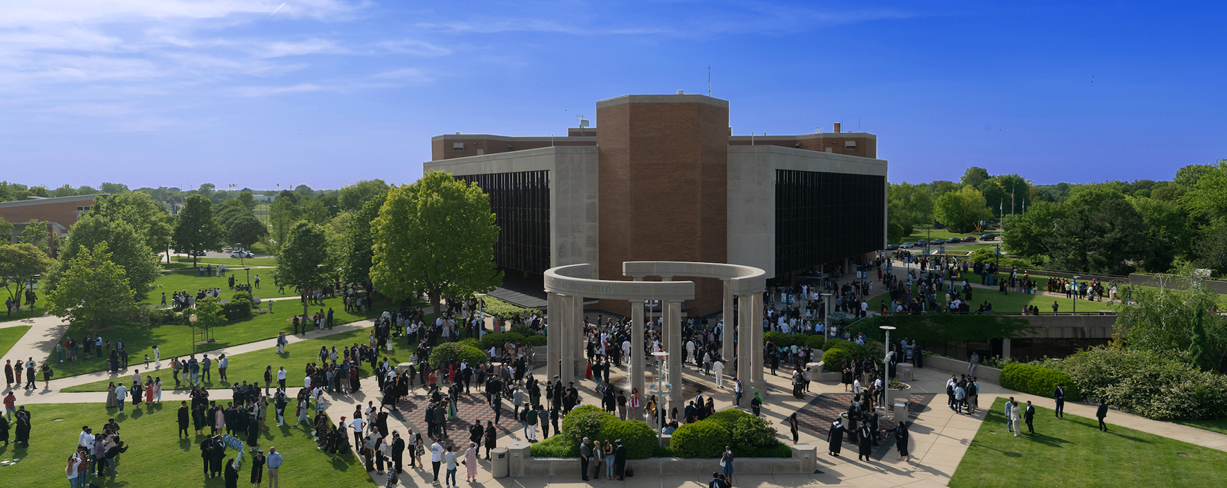 Graduates and families gather at the University of Illinois Springfield colonnade during commencement