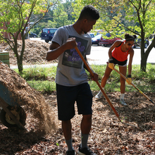 Two members holding a gardening tool and cleaning a natural habitat  
