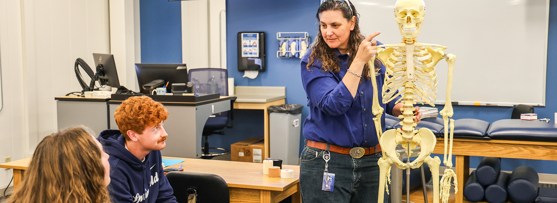 Instructor teaching students with a skeleton model in a classroom setting.