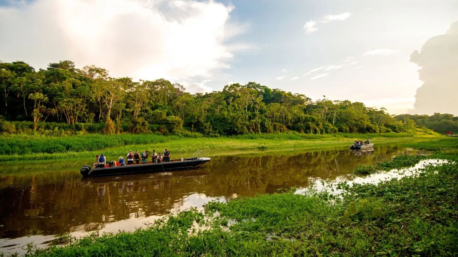 People in the Amazon river in a boat, surrounded by lush greenery under a cloudy sky.