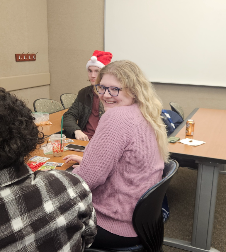 A smiling woman in a purple sweater sitting at a table.