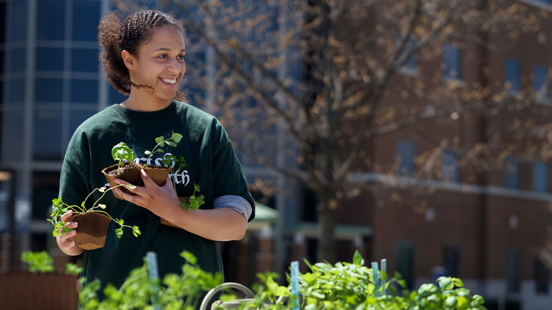 a student holding a plant while standing behind a table filled with other plants