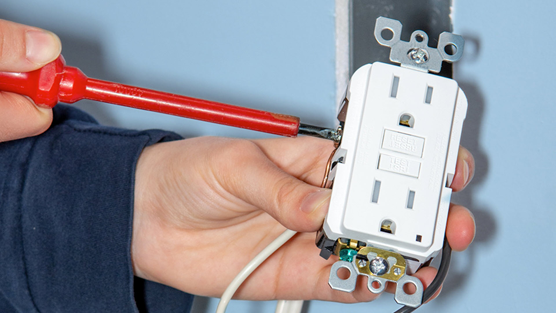 Hands installing an electrical outlet with a red screwdriver.
