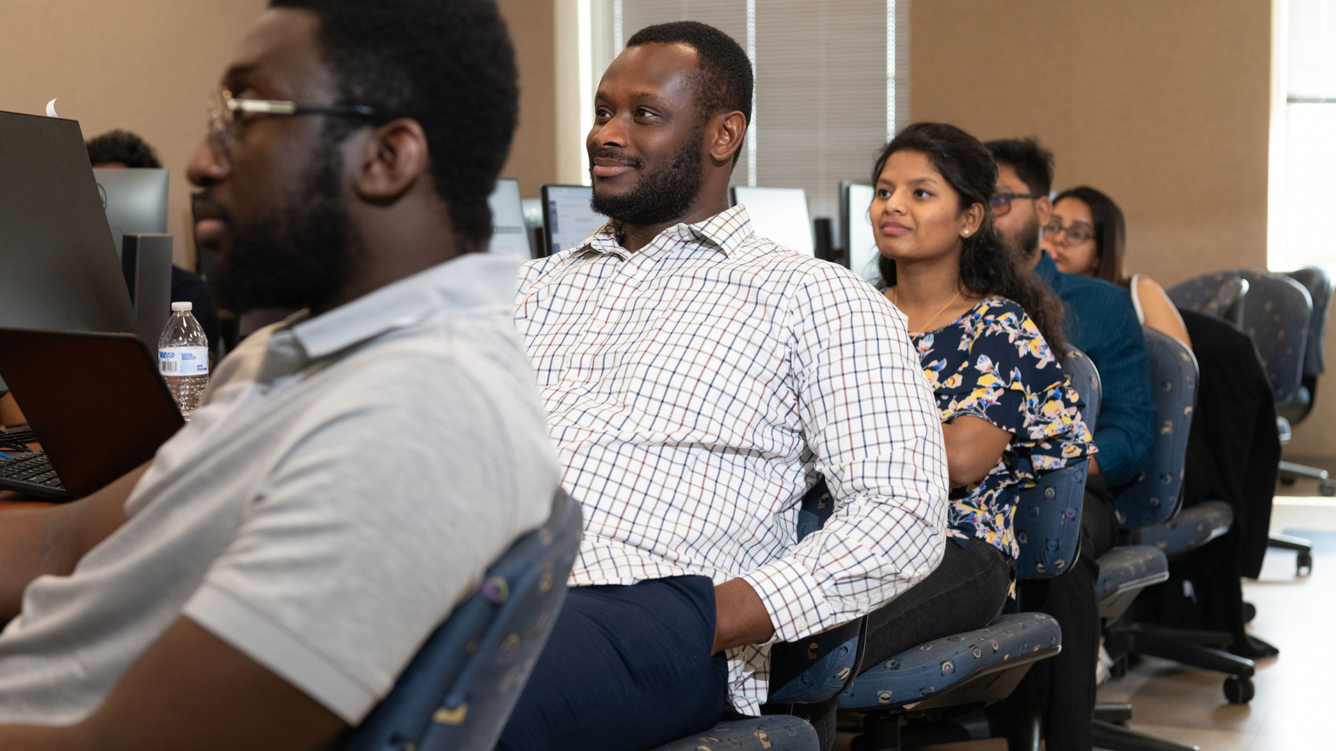 People seated in a classroom, attentively facing forward.