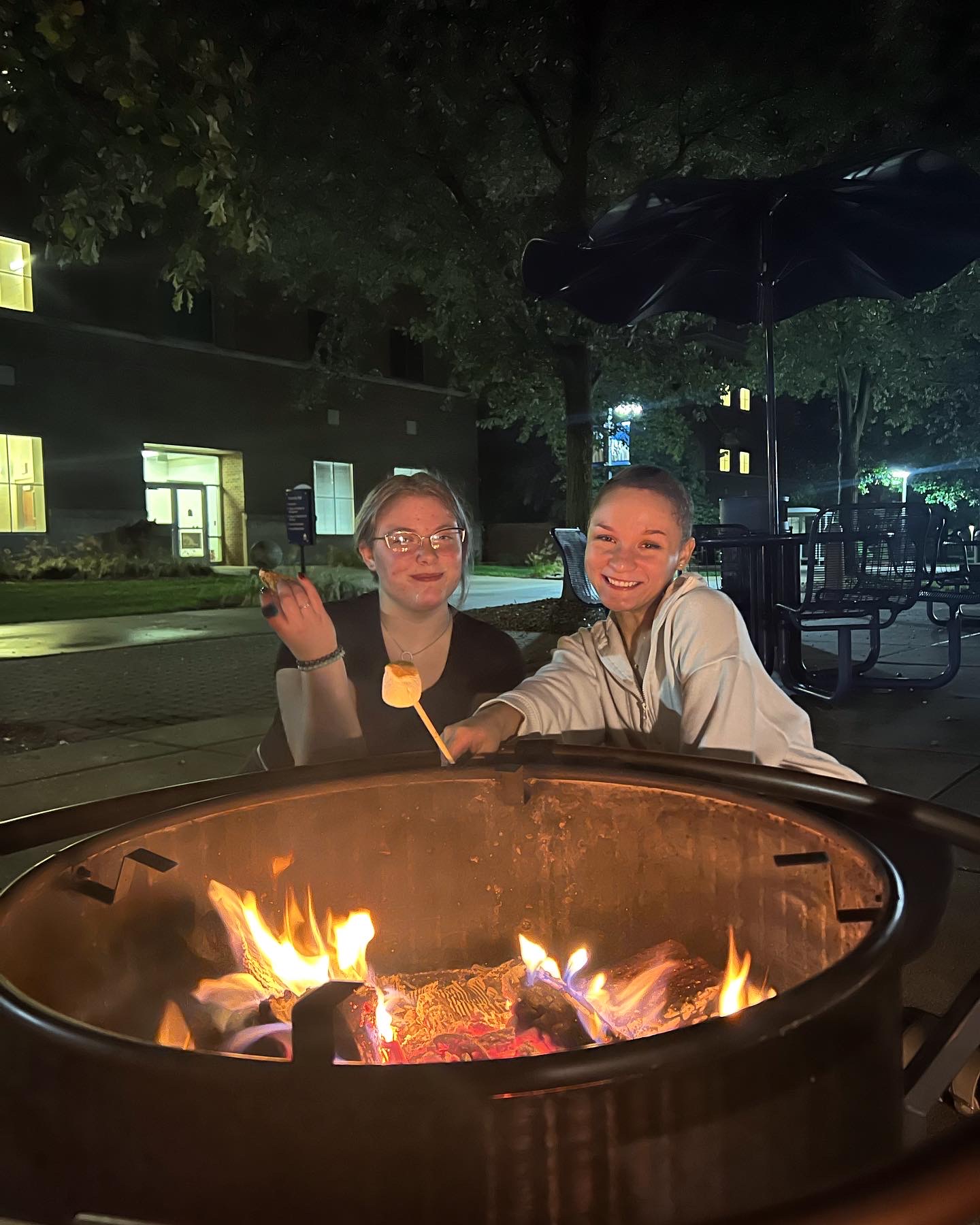 Two students roasting marshmallows over a fire pit.