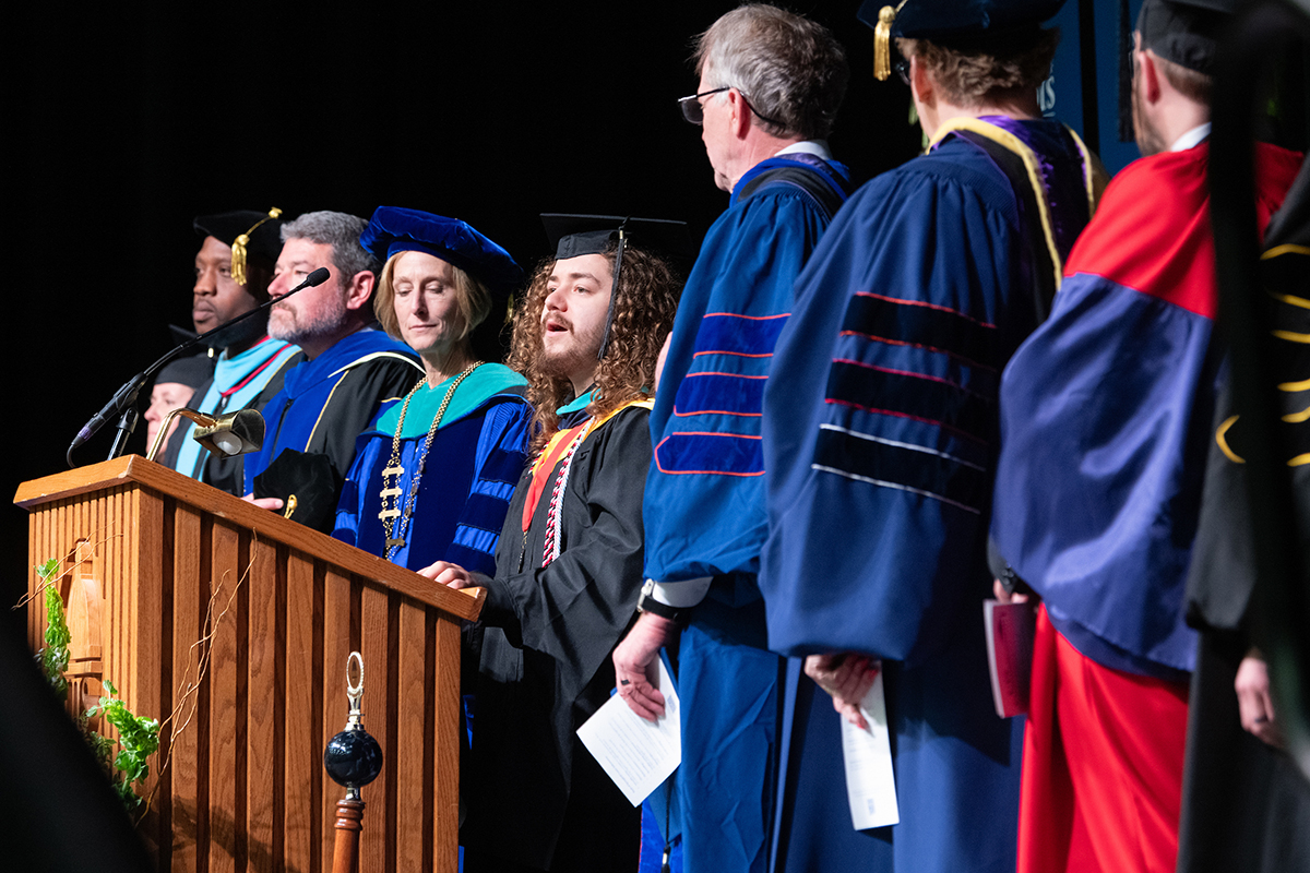 Graduation ceremony with faculty and student on stage.