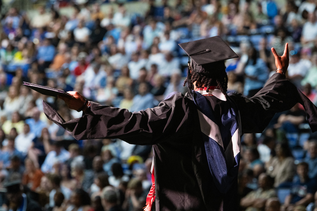 student hands out wide gesturing to the crows with diploma