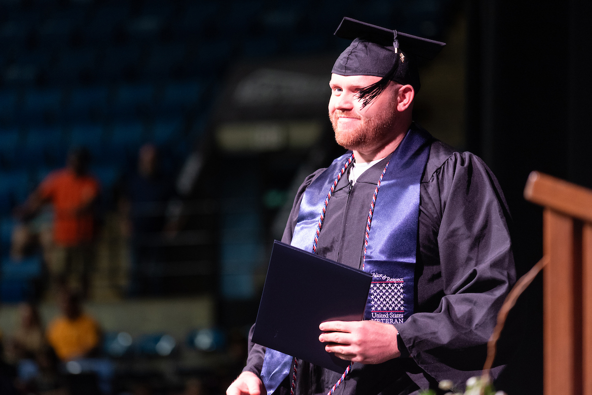 male student smiling at camera walking across stage with diploma
