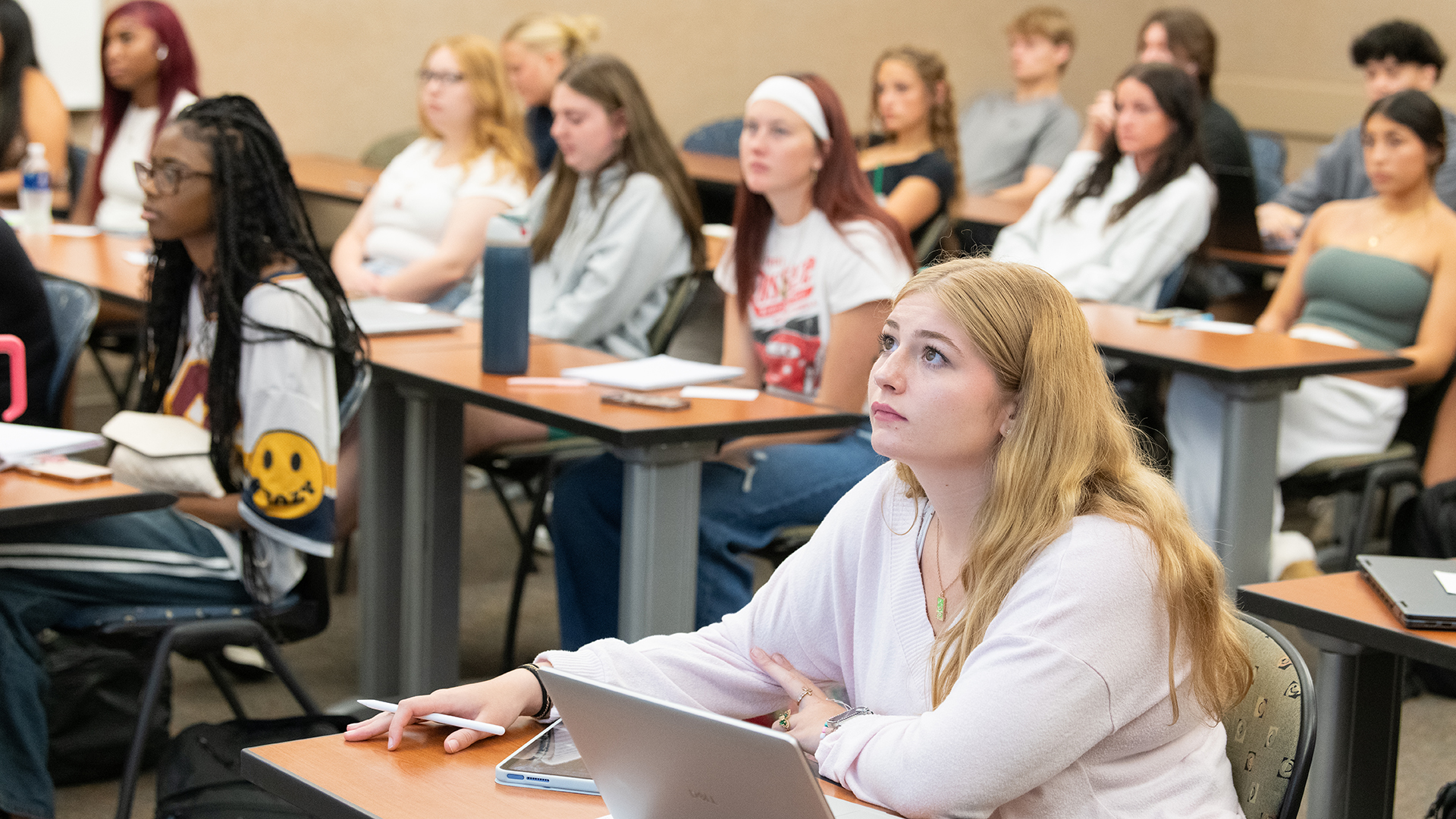Students attentively listening in a classroom, seated at desks.