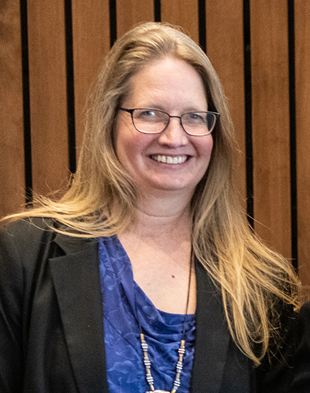Smiling woman with long hair, wearing glasses and a blue top.