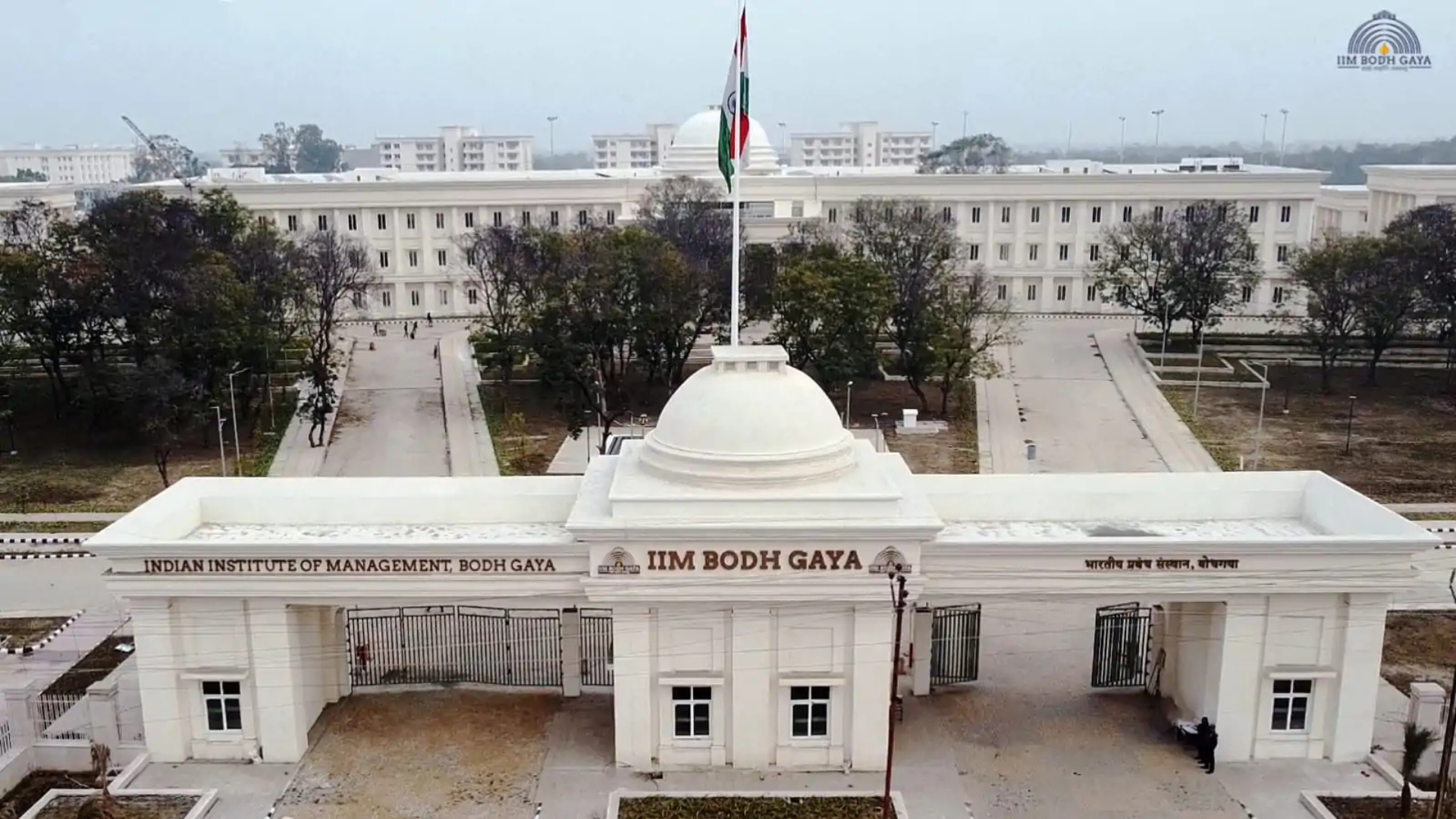 Main entrance gate to IIM, featuring a while domed building with the Indian flag on top.the background.