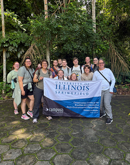 Group of people holding a University of Illinois Springfield banner in a lush, green setting.