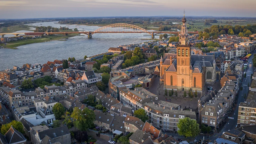 Aerial view of Nijmegen's city center at sunset. Featuring a cathedreal near a river and bridge.