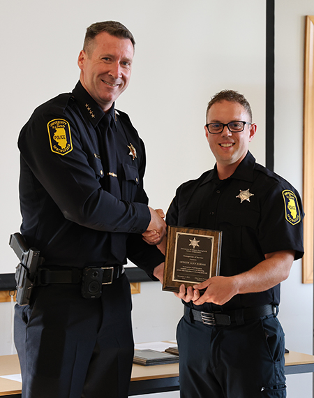Two uniformed officers smiling as one receives a plaque.