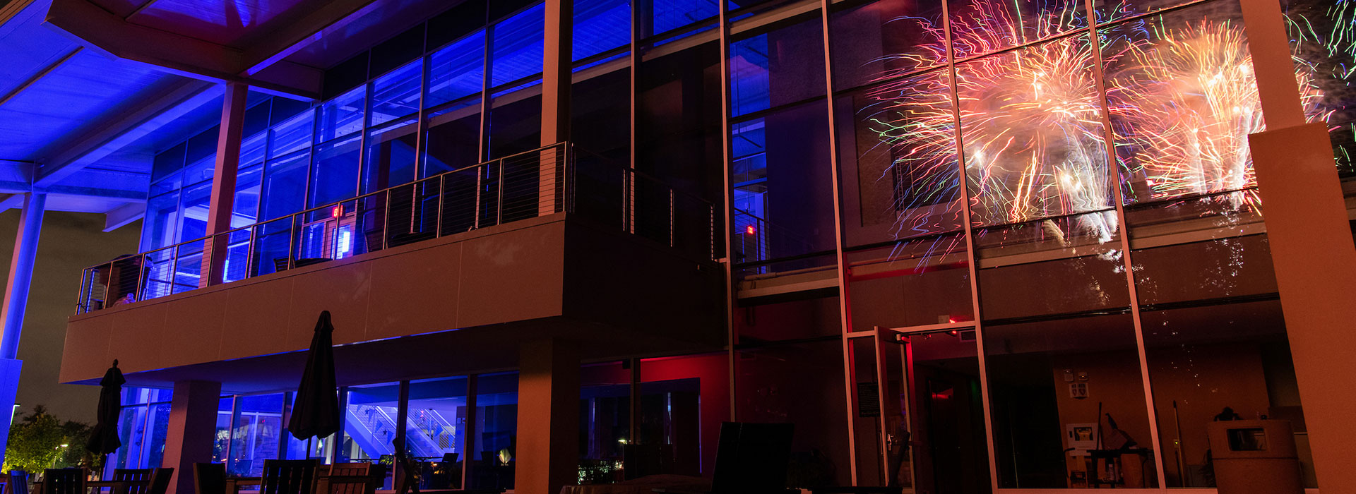 Dark building with blue lighting and bright fireworks in the sky.