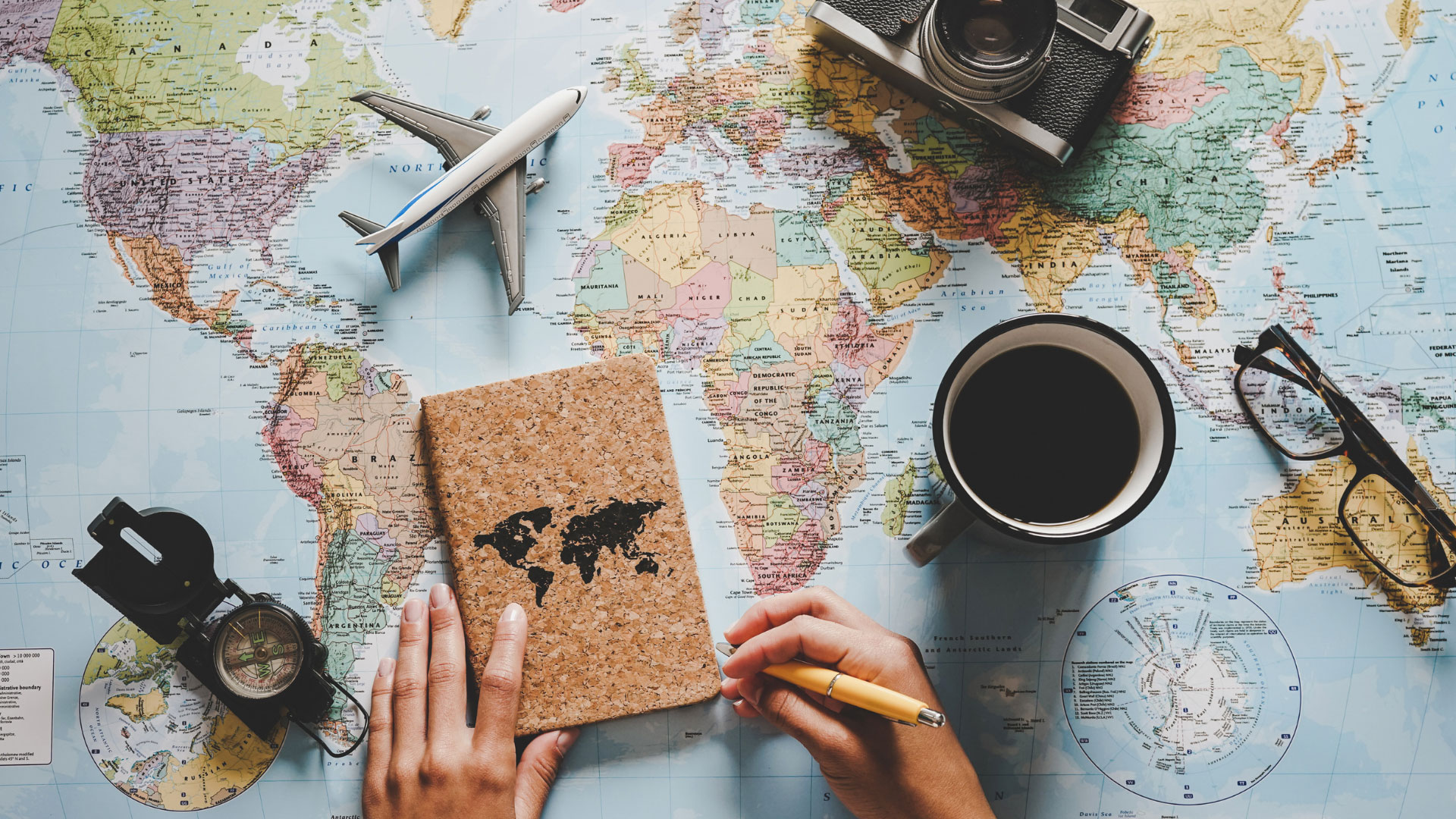 a person writing in a notebook that is on top of a map with travel decor scattered around