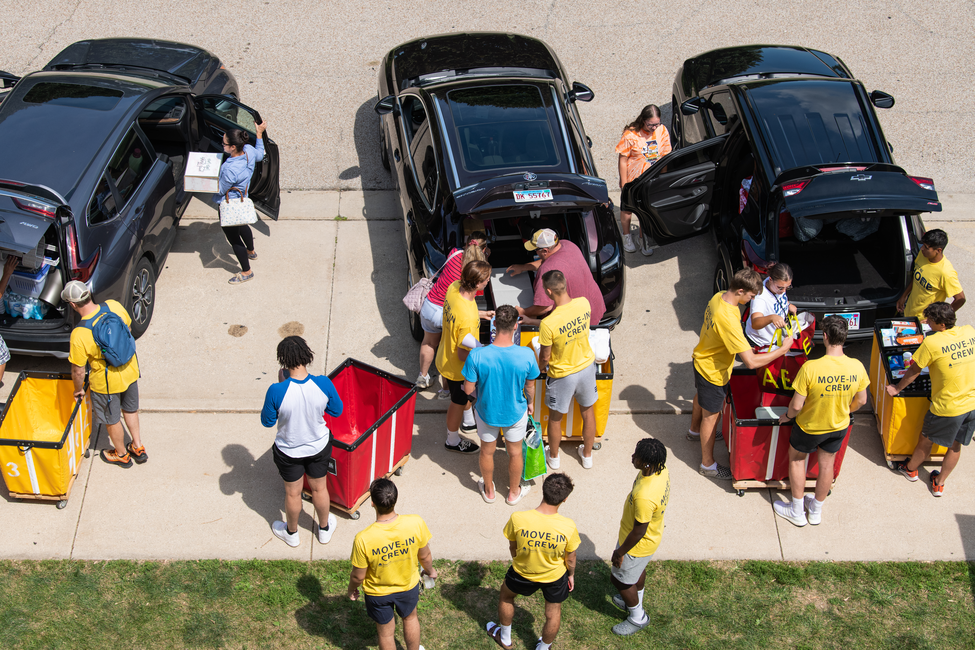 People unloading cars, wearing yellow shirts, outdoor setting.