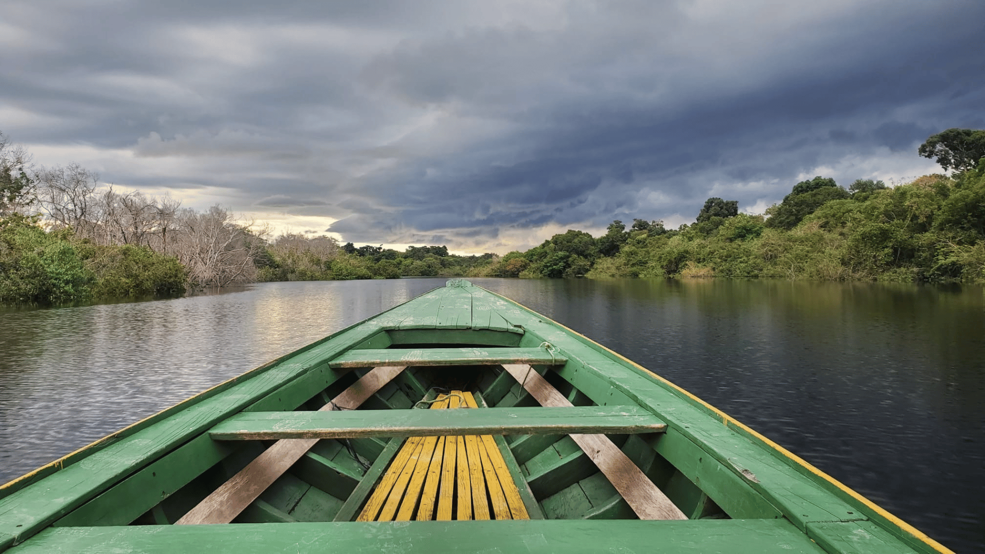 View out of the front of a green boat onto the Amazon river under dramatic skies