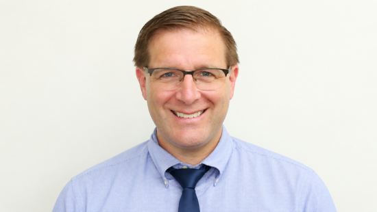 Smiling man wearing glasses, blue shirt, and navy tie.
