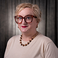 Sarah Adams smiling at the camera with a grey background.