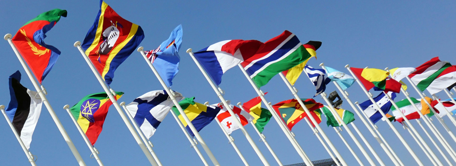 Flags from various countries waving against a clear blue sky.