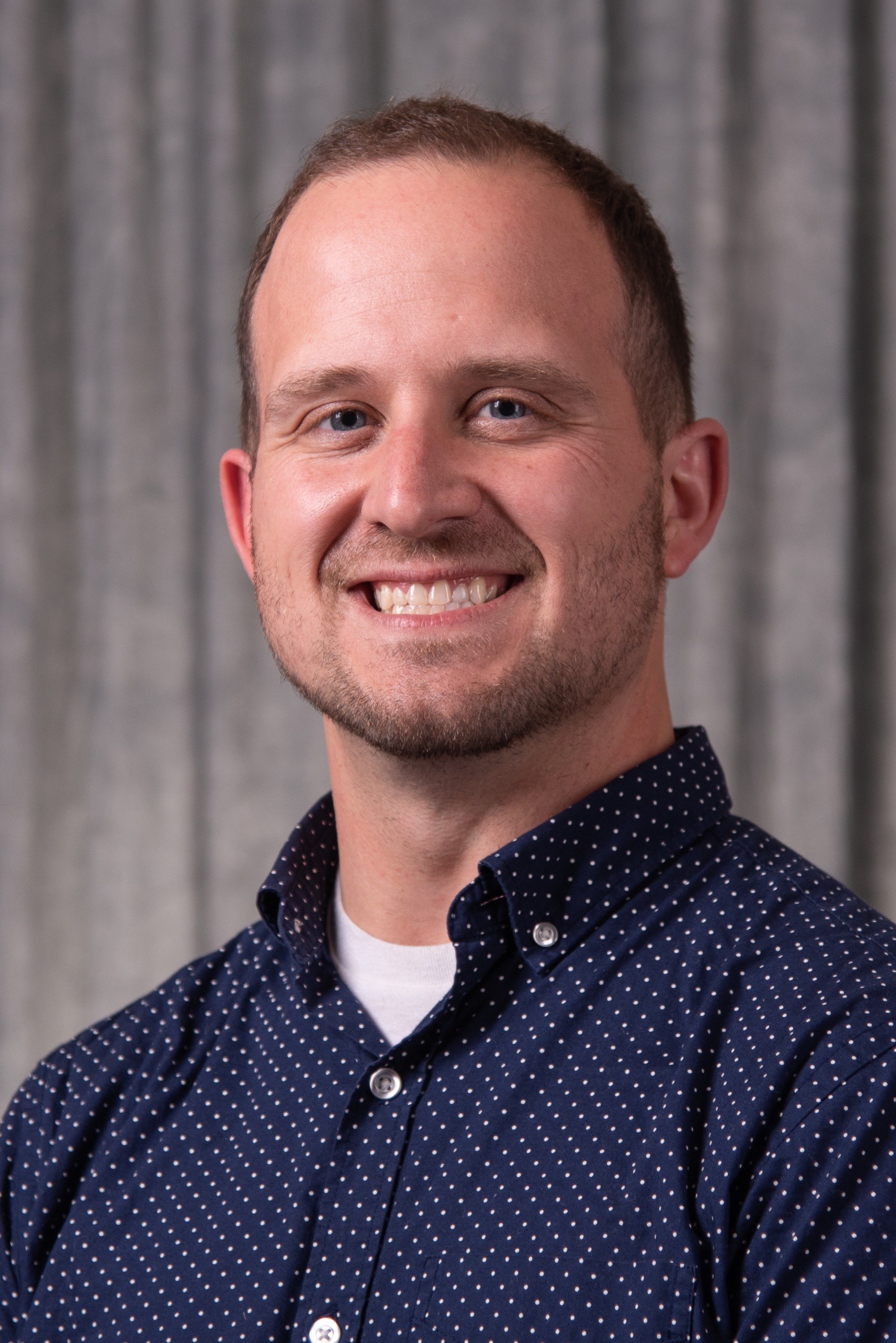 Smiling man in a dark shirt against a gray curtain backdrop, portrait photograph.