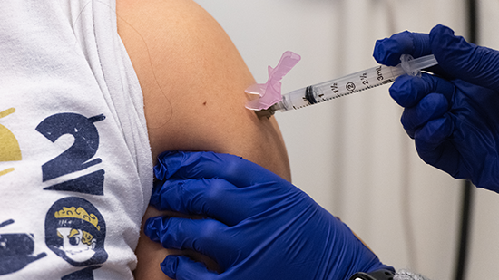 Vaccine injection into an arm by a person wearing blue gloves.