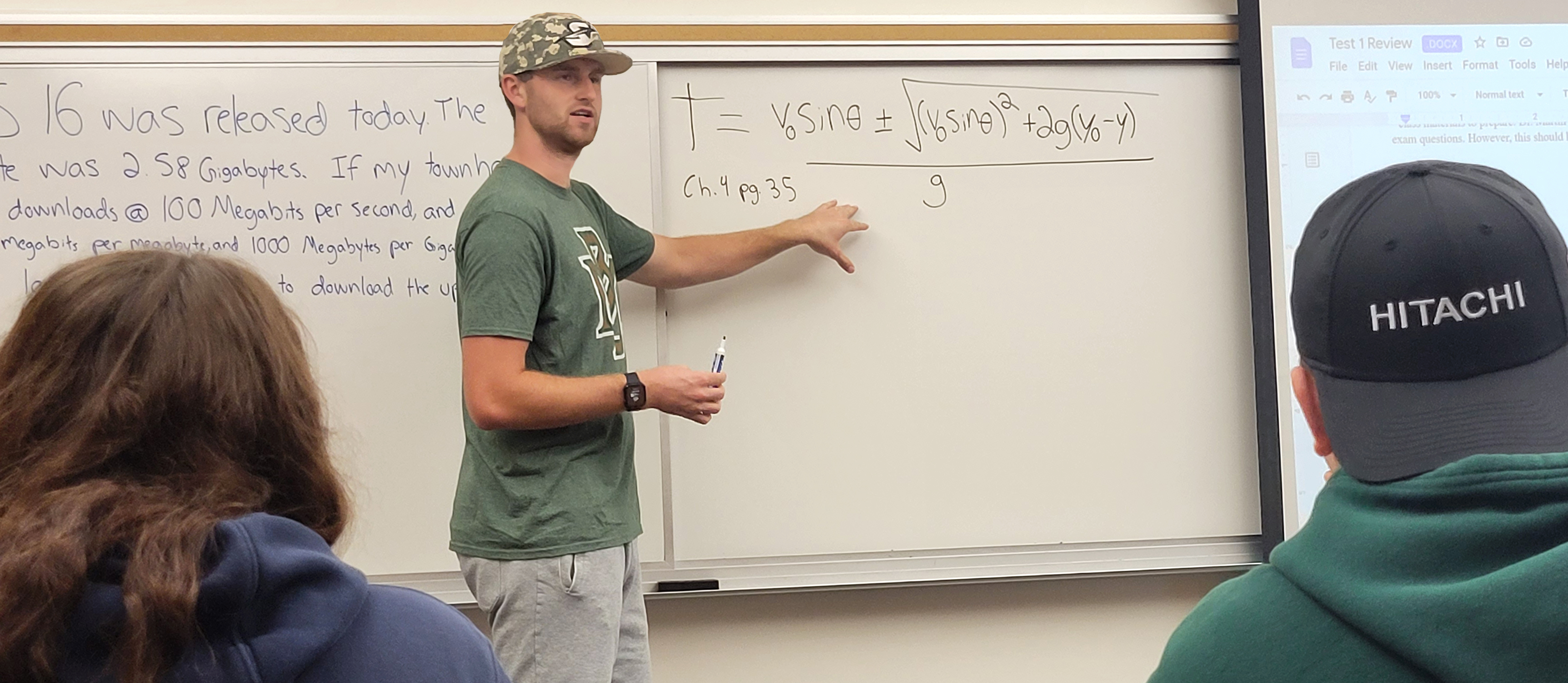 Clark, the Physics S I Leader, covers a sample problem on the white board with his students for their exam review during the S I Session