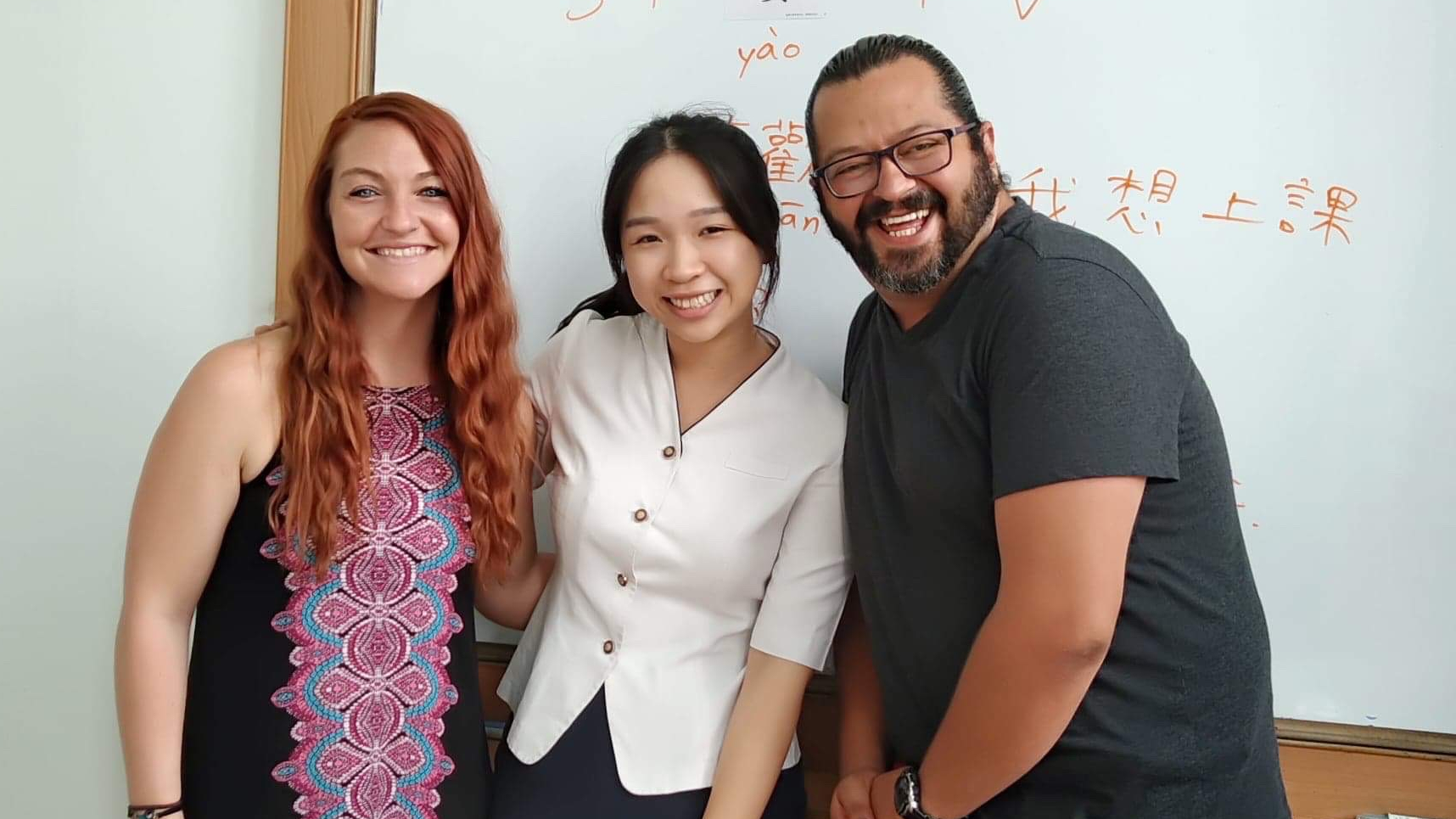 Smiling students and teacher with Chinese lessons on a white board behind them