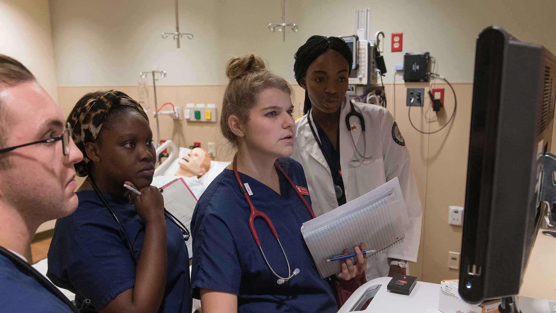 nursing students looking at a computer in nursing simulation lab