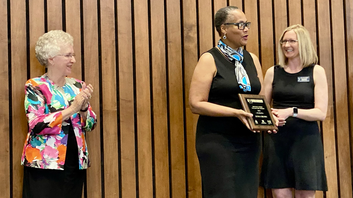 Three people standing on stage, one clapping and another holding an award.