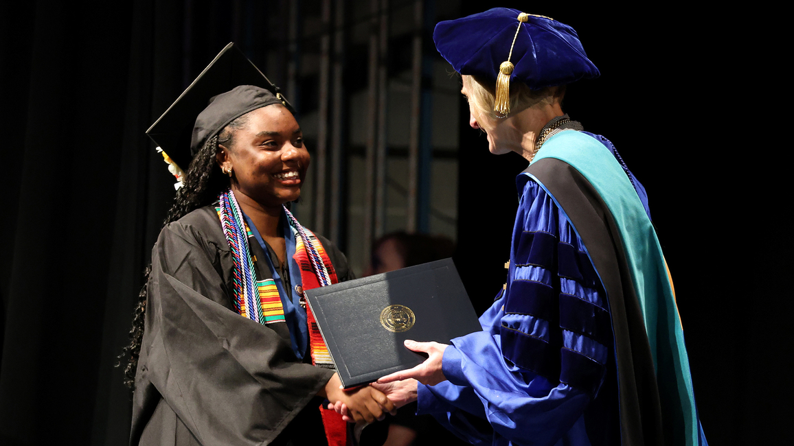 A graduate in cap and gown shakes hands with UIS Chancellor Janet Gooch while holding a diploma cover on stage.