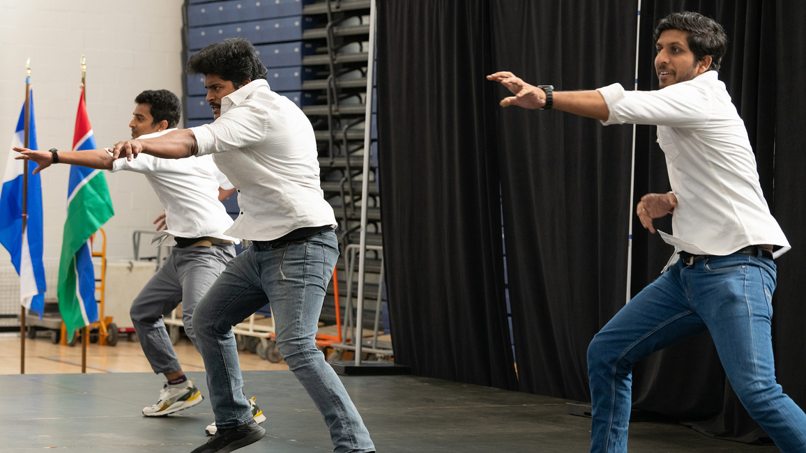 Three people in white shirts and jeans perform a synchronized dance on stage during a cultural event.