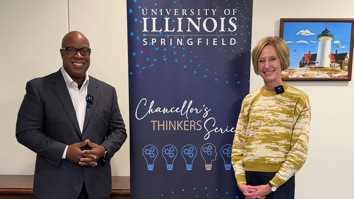 Two people stand smiling near a banner in an indoor setting.