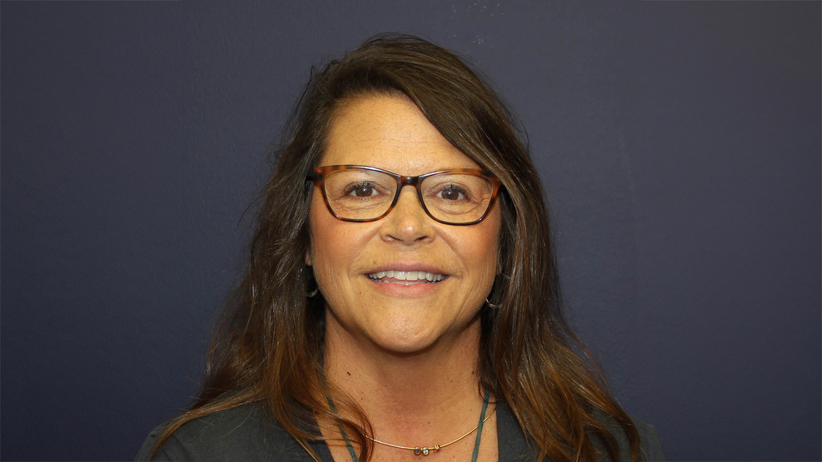 Smiling woman with glasses against a dark background.