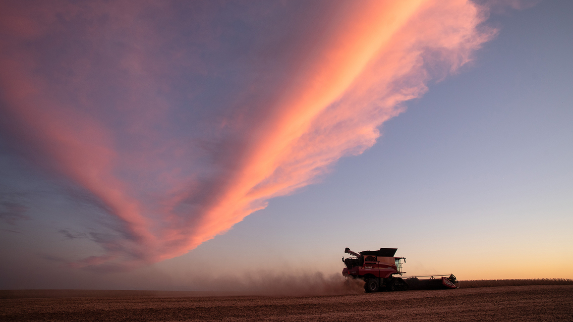 Combine harvester under dramatic red clouds at sunset.