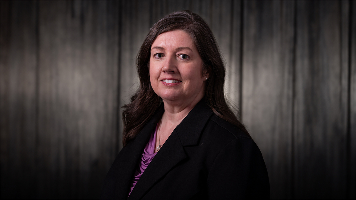Michele Gribbins, a woman in dark attire smiling softly, set against a dimly lit background.
