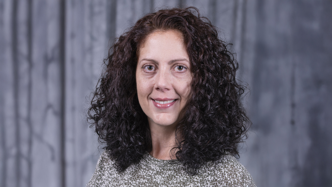 Smiling woman with curly hair on a dark blurred background.