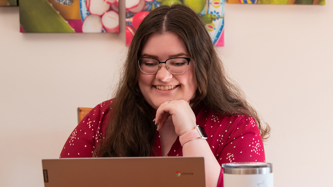 Smiling person using a laptop, colorful artwork in background.