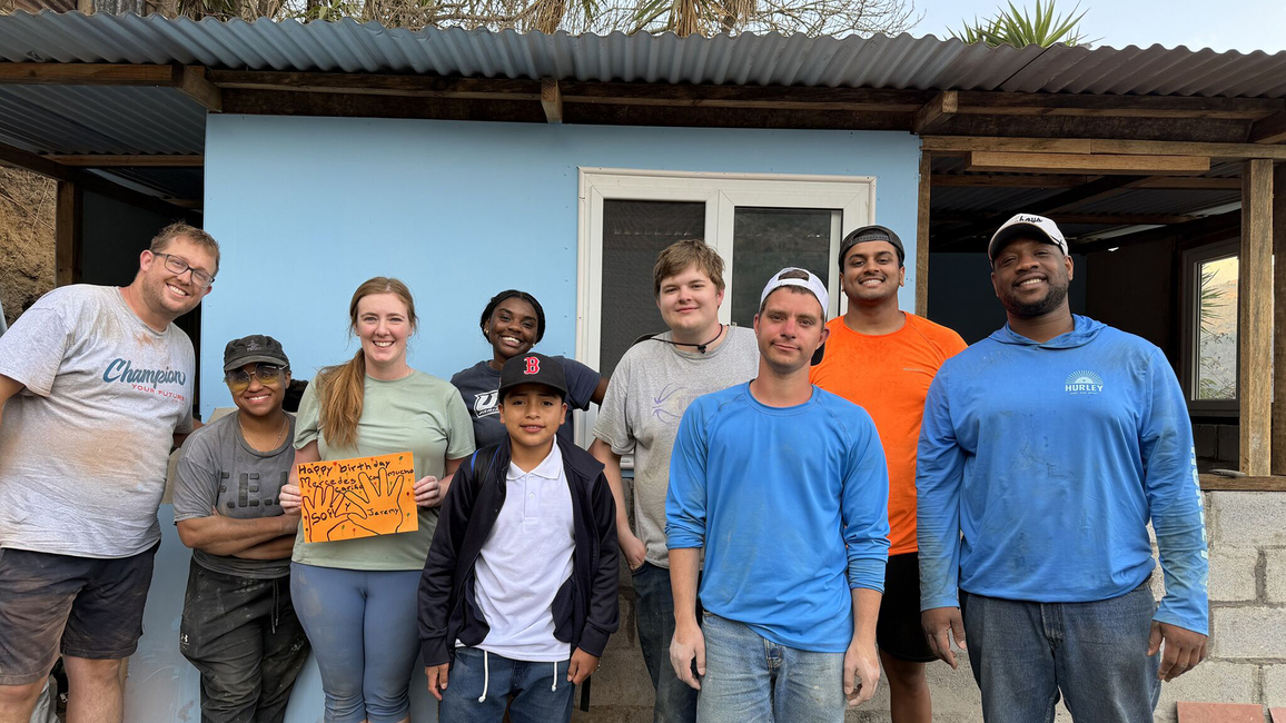 A group of people smiling in front of a light blue house.
