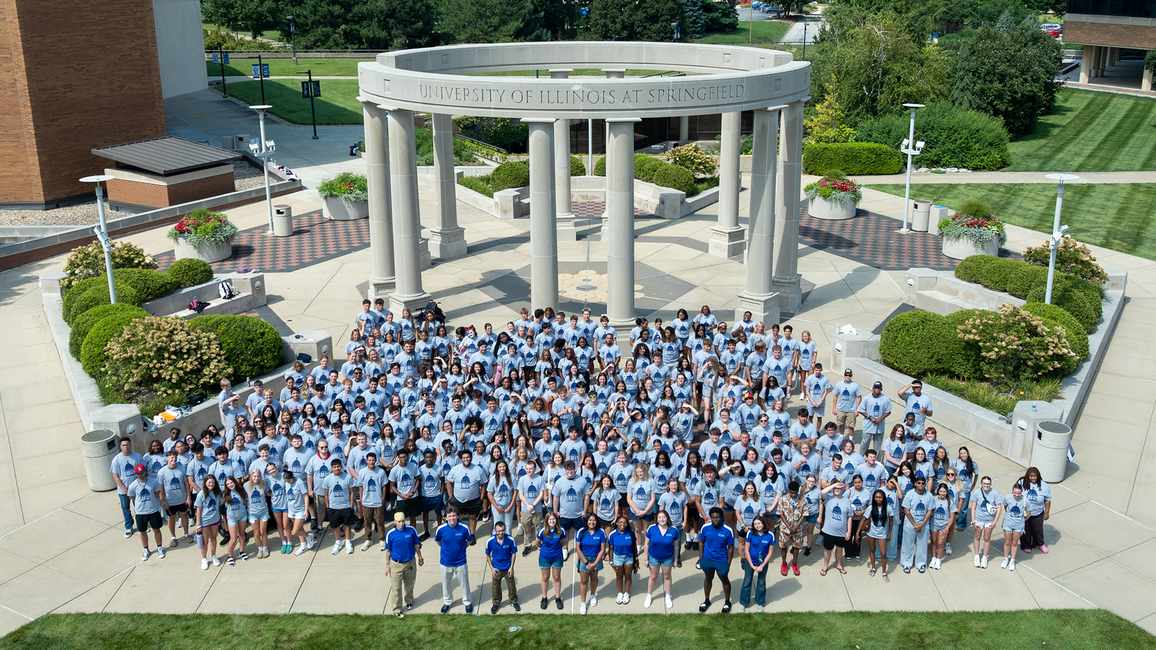 Large group of people in blue shirts gathered outside near circular stone structure.