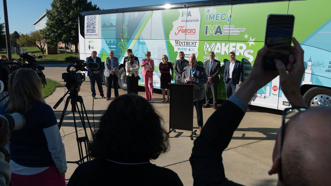 Group of people standing in front of a colorful bus during a sunny event.