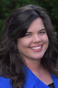 Smiling woman in a blue blouse against a dark background.