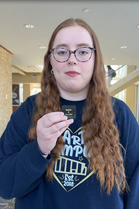 Young woman with glasses holding a small black object indoors.
