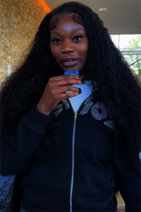 Woman with long curly hair holding a phone, wearing a black jacket.