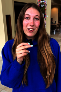 Young woman in a blue hoodie holding a small black object indoors.