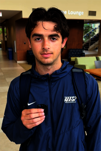 Young man in a blue tracksuit holds a small object in a lounge area.